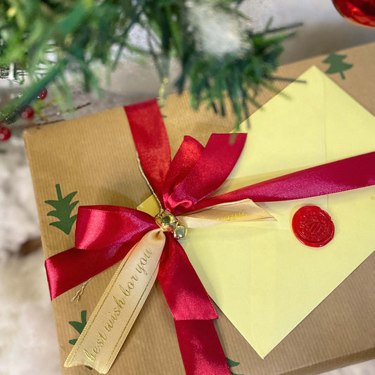 Gift box with red ribbon and gold tag, Christmas tree in background