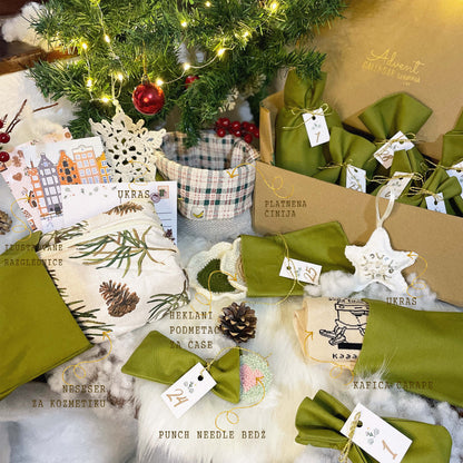 Green decorative items with tags on a textured surface near a Christmas tree.